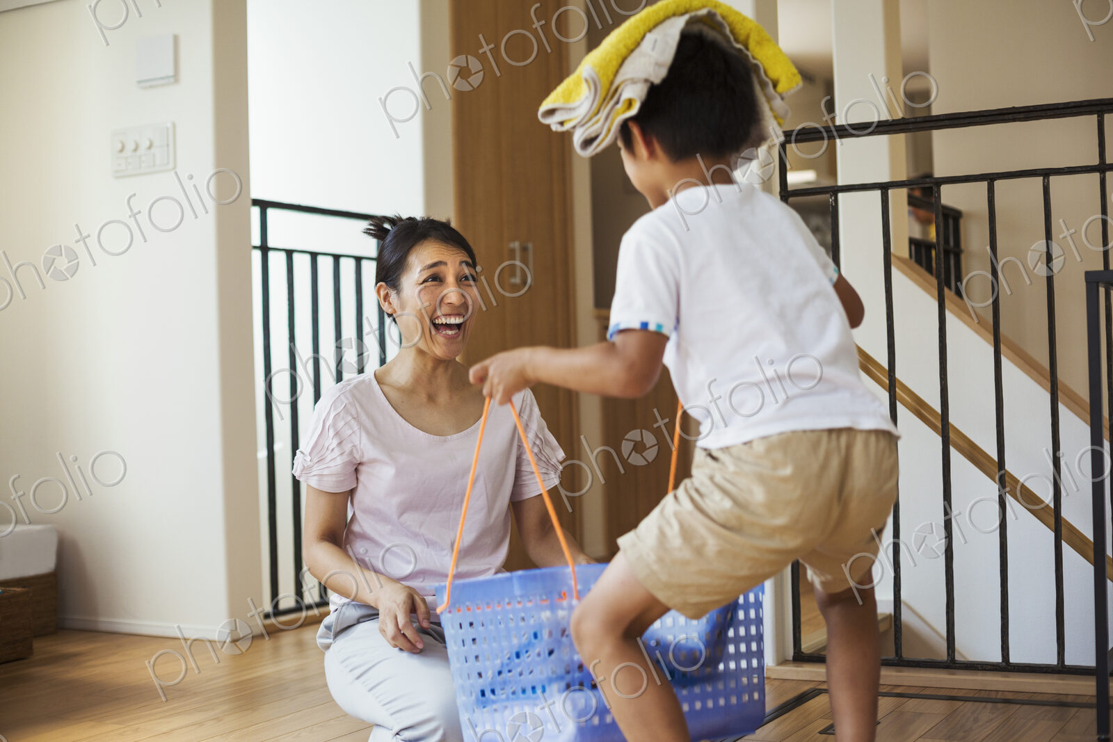 Family home. A woman and her son sorting the laundry, the boy balancing towels on his…