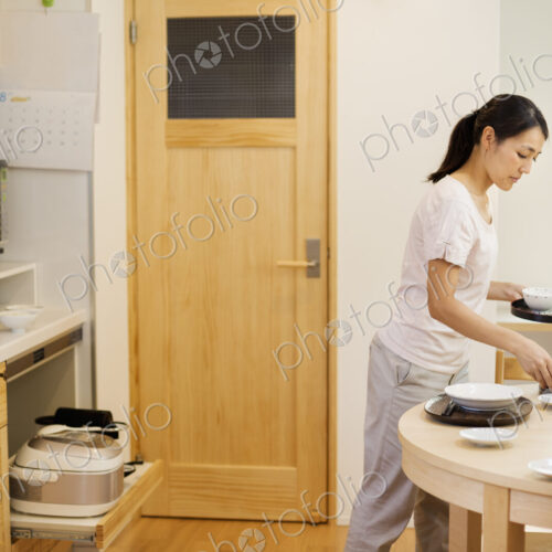 Family home. A woman preparing a meal in a kitchen, placing dishes on the table. Family home. A woman preparing a meal in a kitchen, placing dishes on the table.