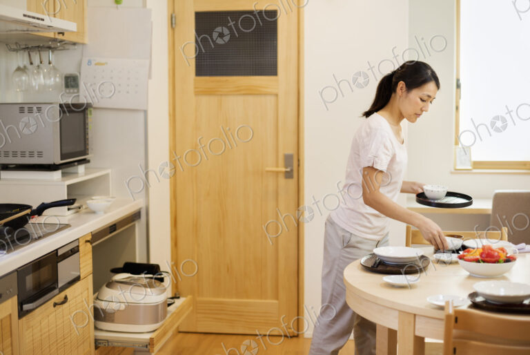 Family home. A woman preparing a meal in a kitchen, placing dishes on the table.