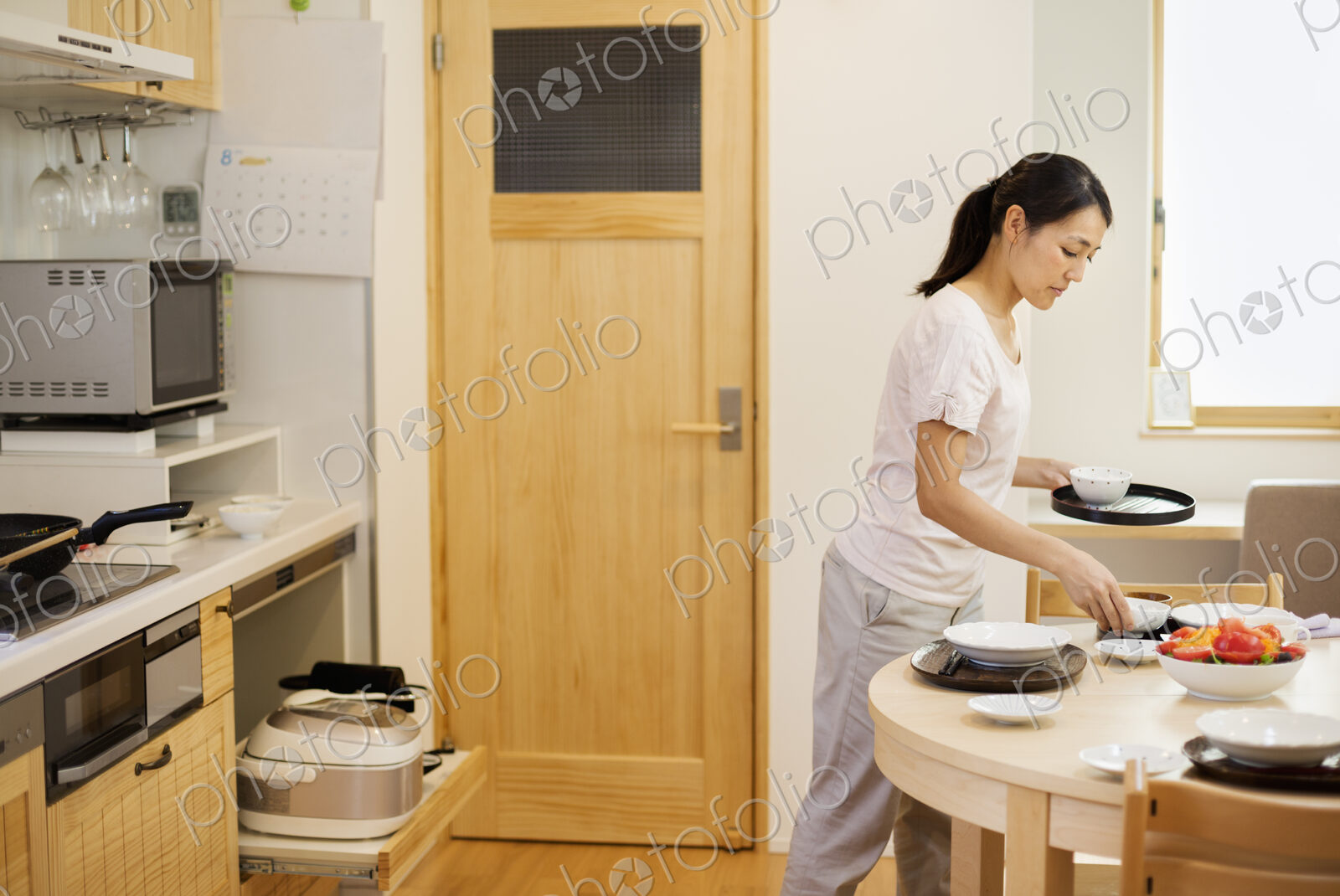 Family home. A woman preparing a meal in a kitchen, placing dishes on the table.