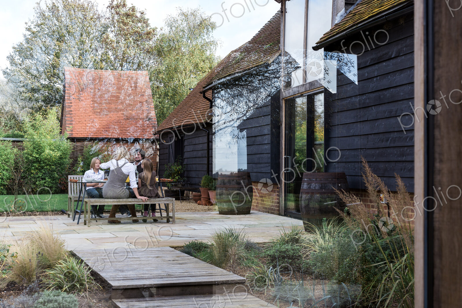 Family sitting at bench outside countryside house.