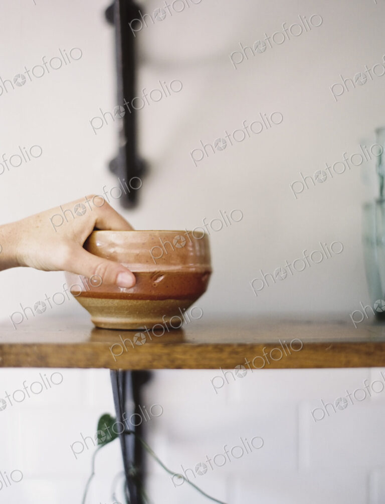 Farm to Table. A person reaching up for a pottery bowl in a domestic kitchen.