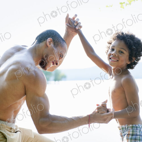 Father playing with his son, wrestling with him by a lake.