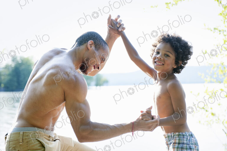 Father playing with his son, wrestling with him by a lake.