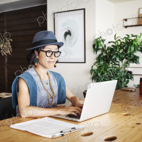 Female Japanese professional sitting at a table in a co-working space, using laptop… Female Japanese professional sitting at a table in a co-working space, using laptop…