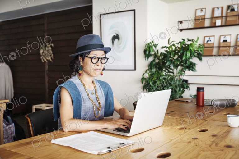 Female Japanese professional sitting at a table in a co-working space, using laptop…