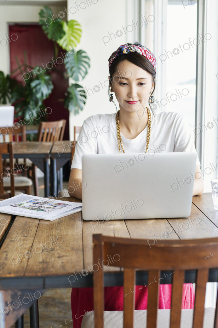 Female Japanese professional sitting at a table in a co-working space, using laptop…