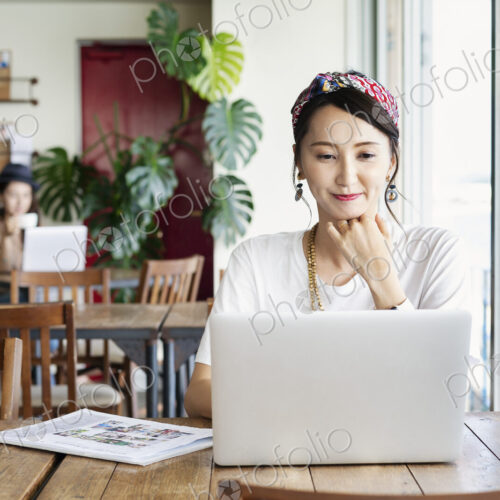 Female Japanese professional sitting at a table in a co-working space, using laptop…