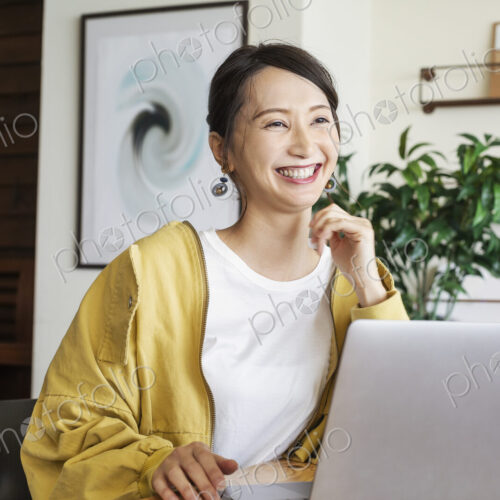 Female Japanese professional sitting at a table in a co-working space, using laptop…