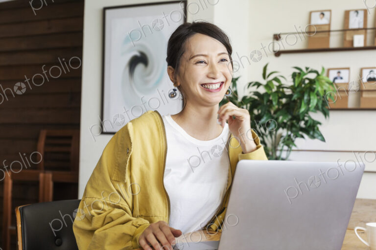 Female Japanese professional sitting at a table in a co-working space, using laptop…