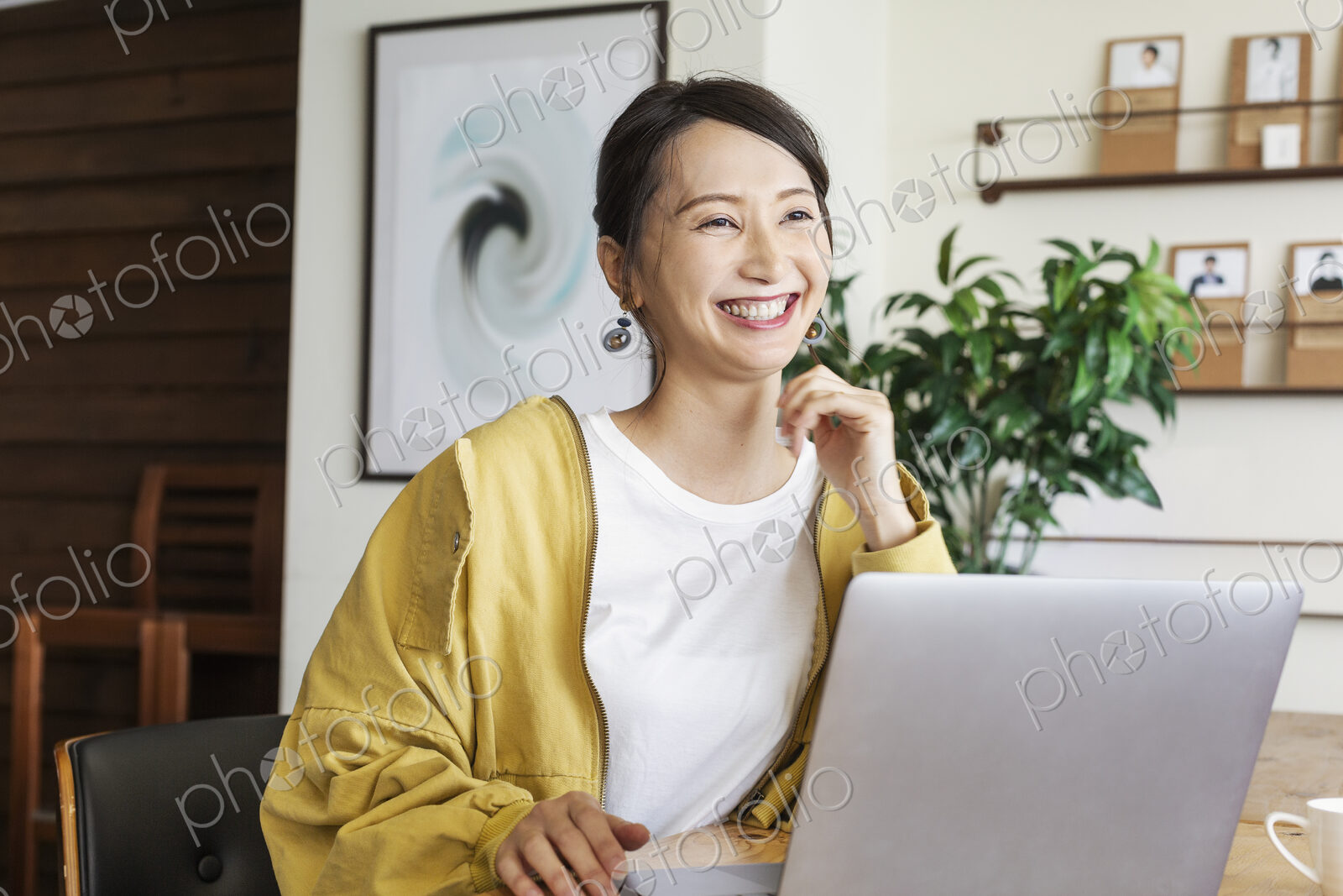 Female Japanese professional sitting at a table in a co-working space, using laptop…