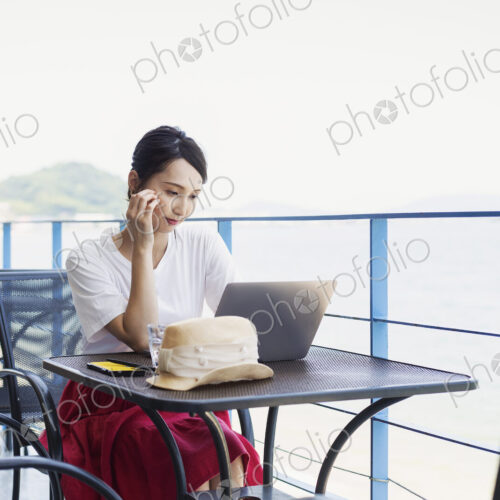 Female Japanese professional sitting on balcony of a co-working space, using laptop…