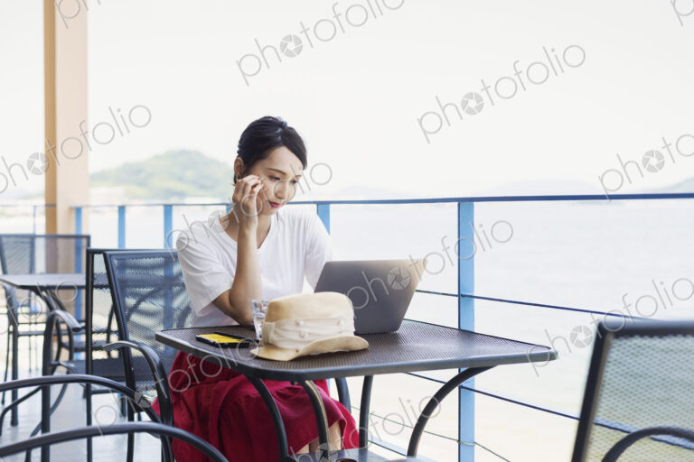 Female Japanese professional sitting on balcony of a co-working space, using laptop…