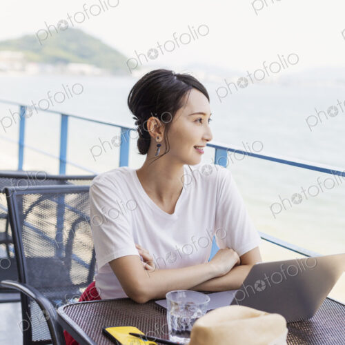 Female Japanese professional sitting on balcony of a co-working space, using laptop…