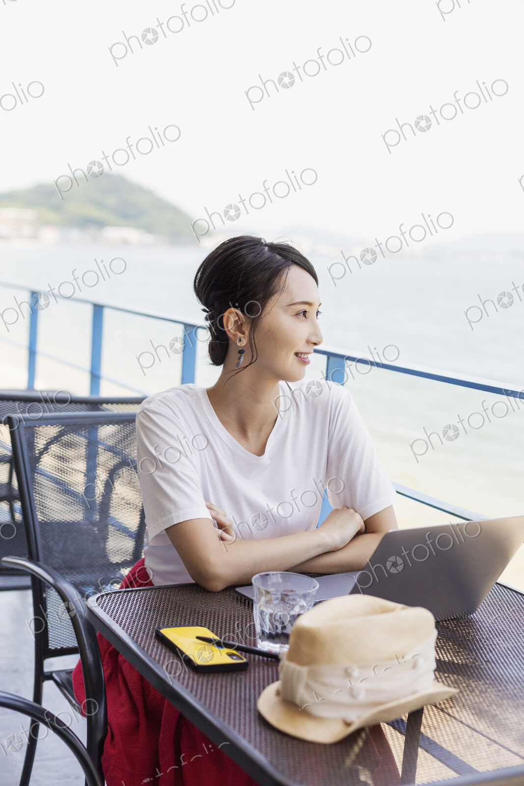 Female Japanese professional sitting on balcony of a co-working space, using laptop…