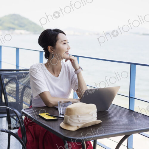 Female Japanese professional sitting on balcony of a co-working space, using laptop…
