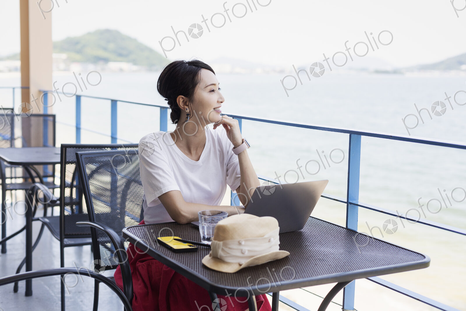 Female Japanese professional sitting on balcony of a co-working space, using laptop…