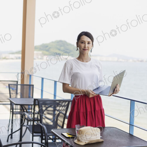 Female Japanese professional standing on balcony of a co-working space, holding laptop…