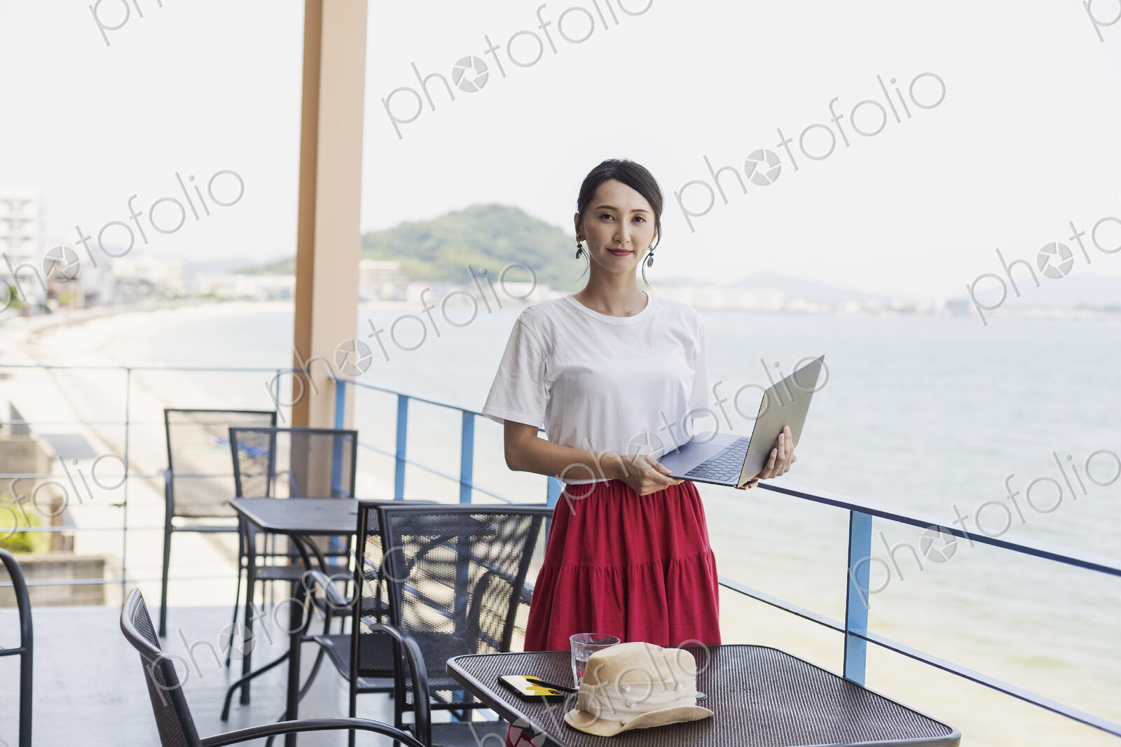 Female Japanese professional standing on balcony of a co-working space, holding laptop…