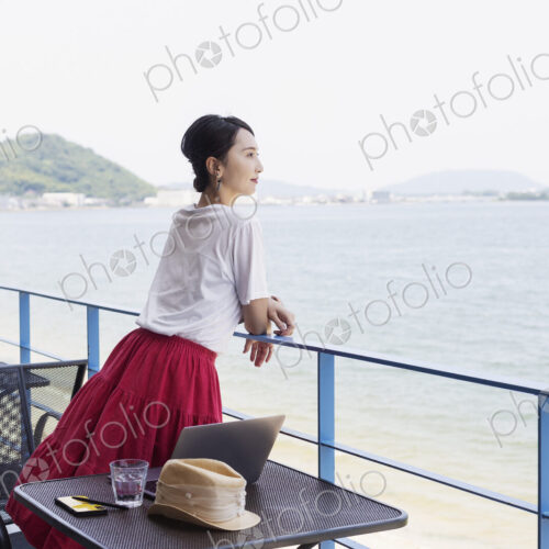 Female Japanese professional standing on balcony of a co-working space, laptop…