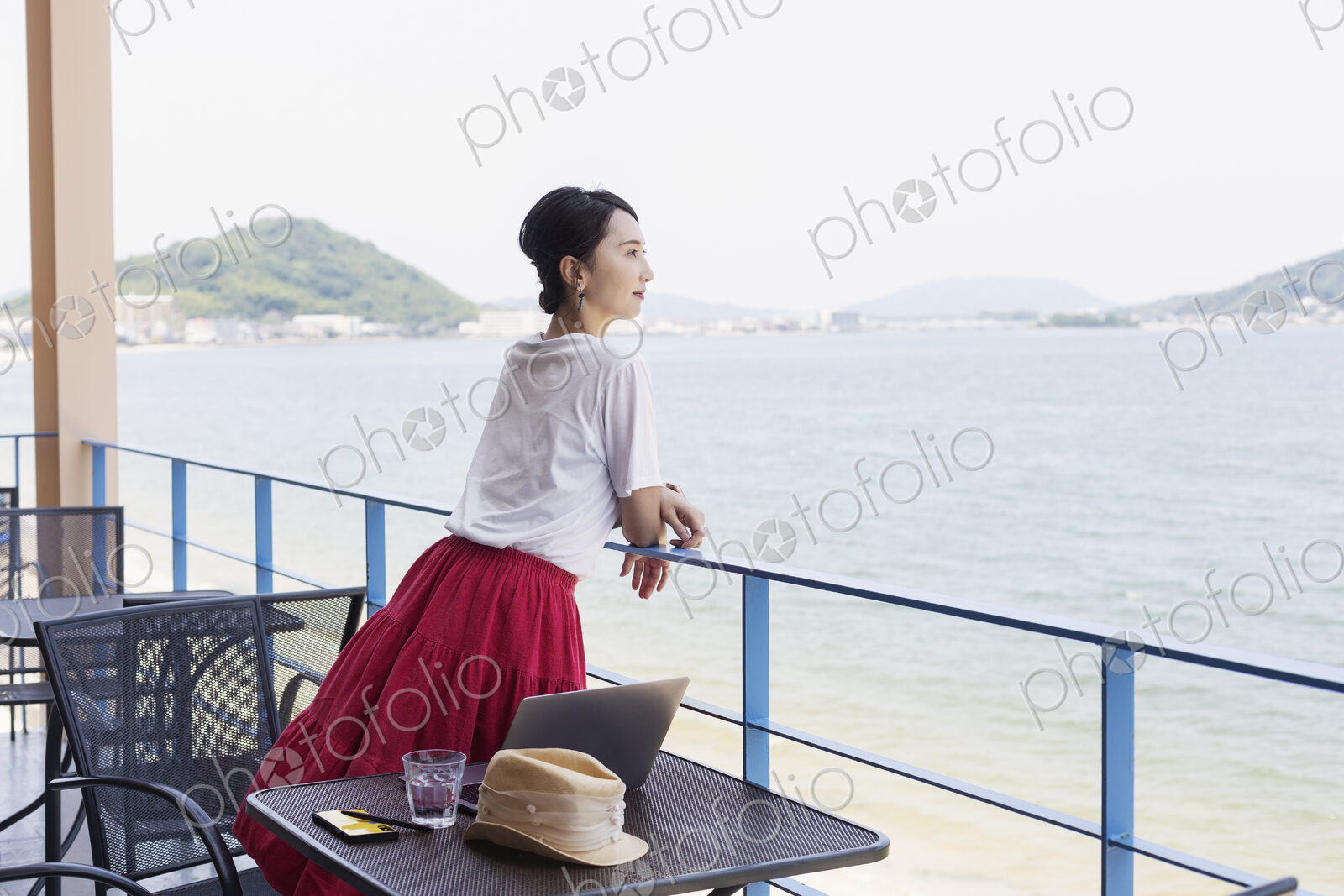Female Japanese professional standing on balcony of a co-working space, laptop…