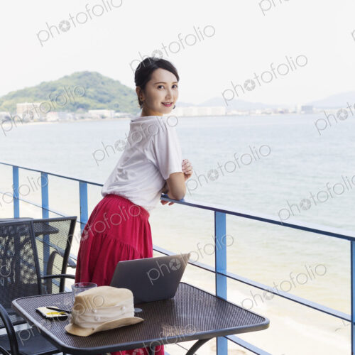 Female Japanese professional standing on balcony of a co-working space, laptop…