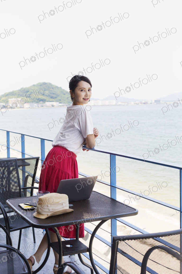 Female Japanese professional standing on balcony of a co-working space, laptop…