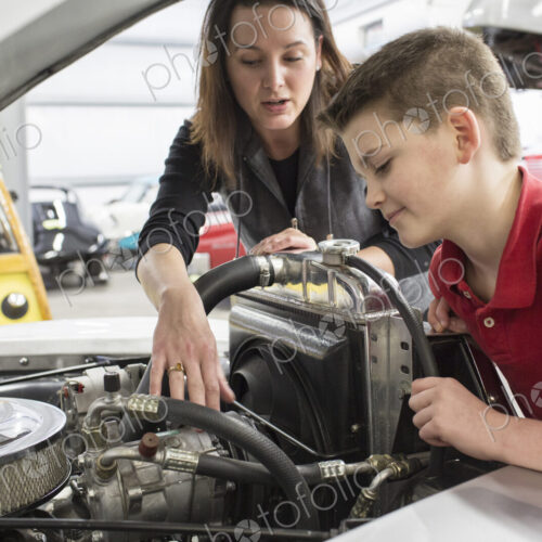 Female car mechanic and boy looking at a classic car engine.