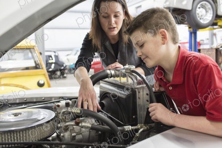 Female car mechanic and boy looking at a classic car engine.