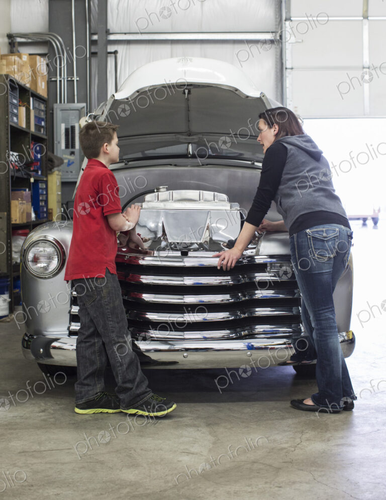 Female car mechanic talks to a boy about a car engine in a classic car repair shop.