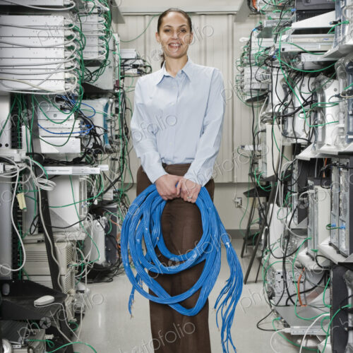 Female computer technician holding CAT 5 cables and standing in the aisle of a… Female computer technician holding CAT 5 cables and standing in the aisle of a…