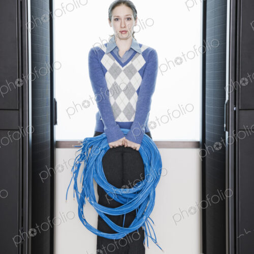 Female computer technician holding CAT 5 cables and standing in the aisle of a… Female computer technician holding CAT 5 cables and standing in the aisle of a…