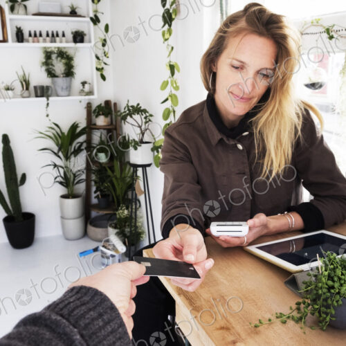 Female owner of plant shop receiving credit card from customer for payment of small… Female owner of plant shop receiving credit card from customer for payment of small…