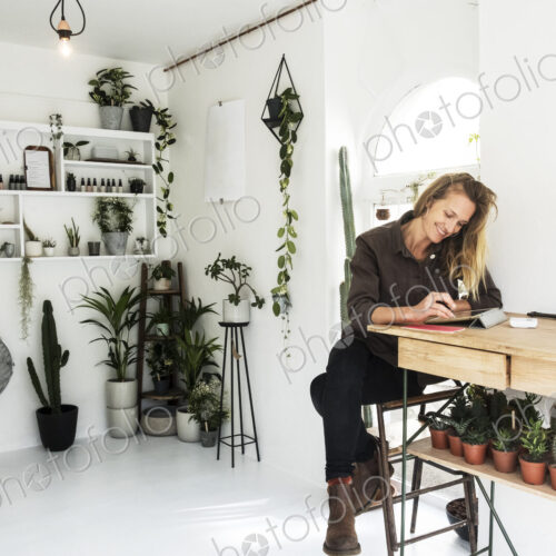 Female owner of plant shop sitting at table, working on digital tablet, a selection of… Female owner of plant shop sitting at table, working on digital tablet, a selection of…