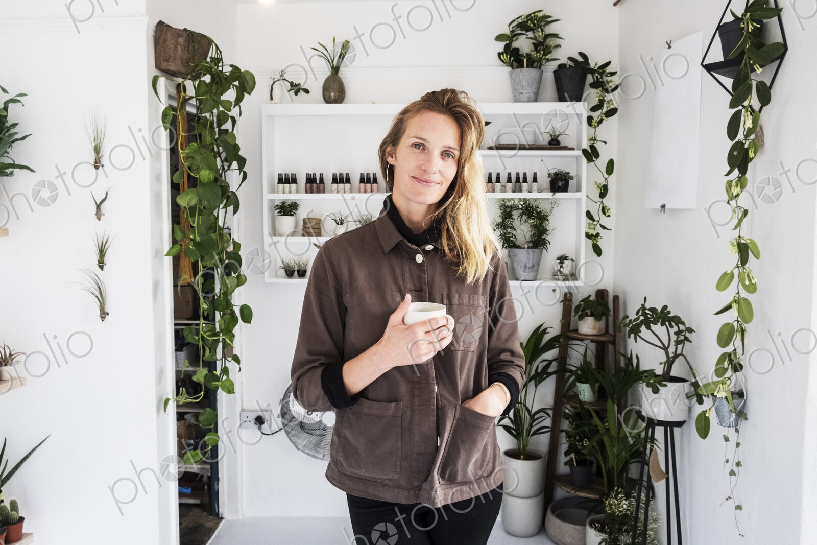 Female owner of plant shop smiling at camera, a selection of plants on wooden shelves.
