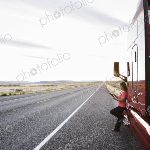 Female truck driver standing next to the cab of her truck near the highway in eastern… Female truck driver standing next to the cab of her truck near the highway in eastern…