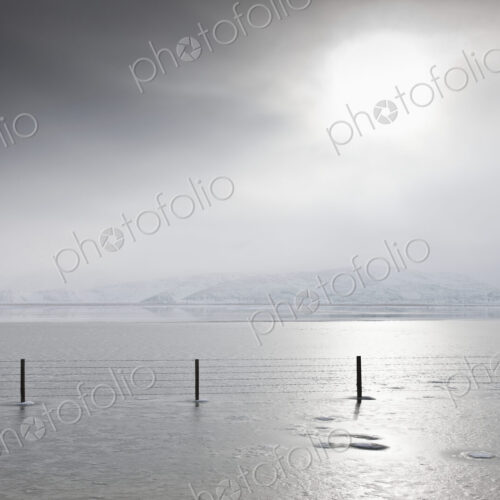 Fence in wintry landscape with grey sky.