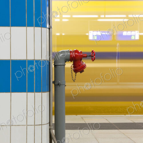 Fire hydrant on a pillar at a train station with a passing train in the background.