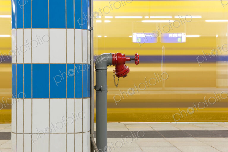 Fire hydrant on a pillar at a train station with a passing train in the background.