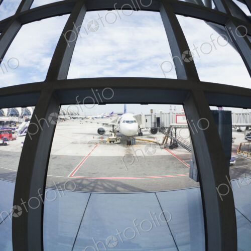 Fish eye lens view of airplanes parked on airport tarmac from terminal window.