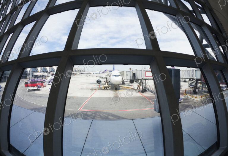 Fish eye lens view of airplanes parked on airport tarmac from terminal window.