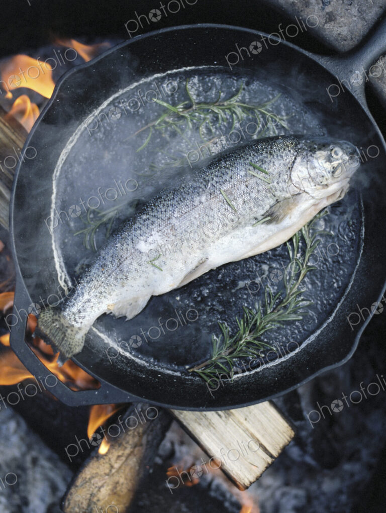 Fish in a frying pan over an outdoor fire.