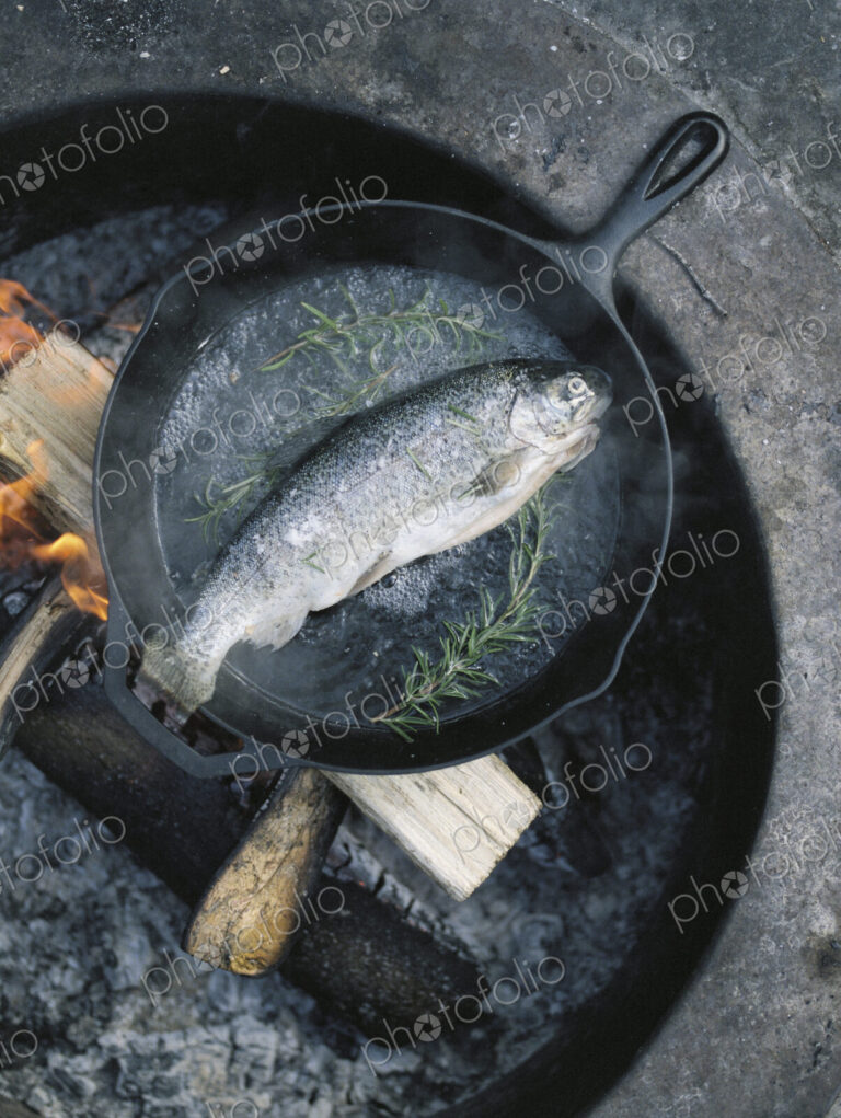 Fish in a frying pan over an outdoor fire.