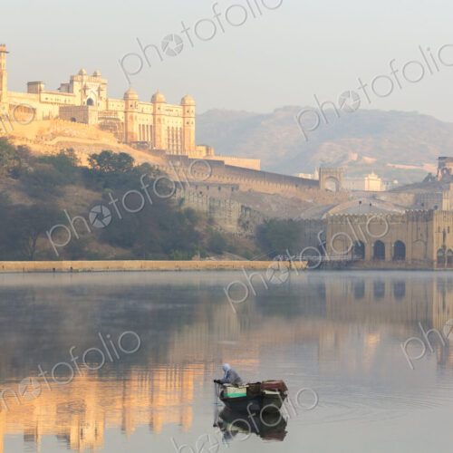 Fisherman in boat on calm lake at sunrise, large fort on hill in the distance. Fisherman in boat on calm lake at sunrise, large fort on hill in the distance.
