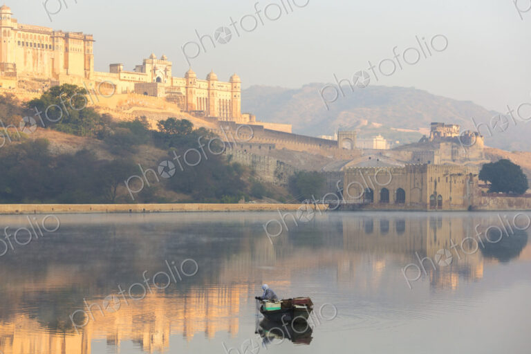Fisherman in boat on calm lake at sunrise, large fort on hill in the distance.