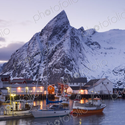 Fishing boats moored in harbour of settlement, with snow-capped mountains behind. Fishing boats moored in harbour of settlement, with snow-capped mountains behind.