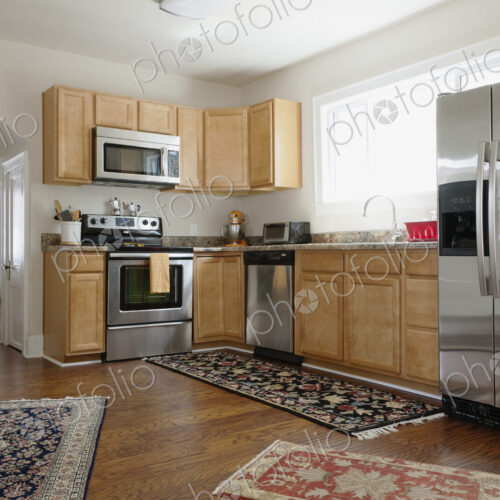 Fitted kitchen in a modern home, ovens and integrated appliances, fridge and rugs on a…