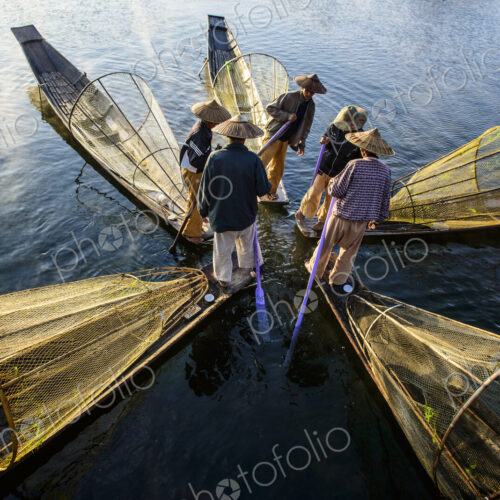 Five fishermen on traditional boats with conical fishing nets.