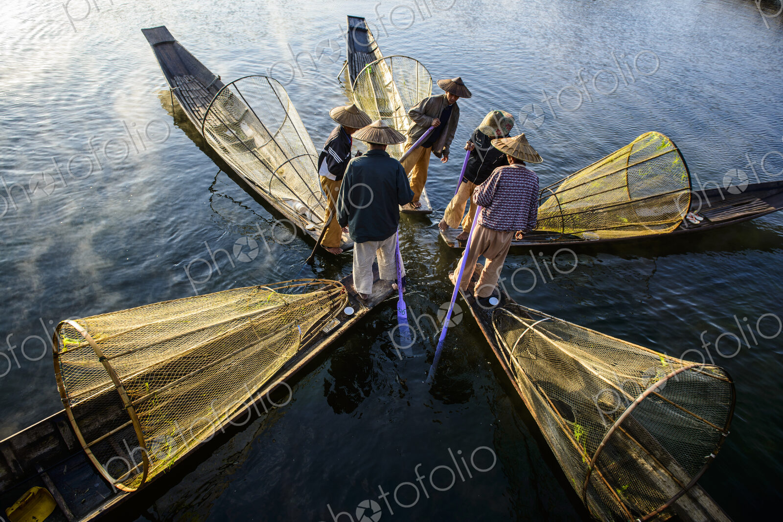 Five fishermen on traditional boats with conical fishing nets.