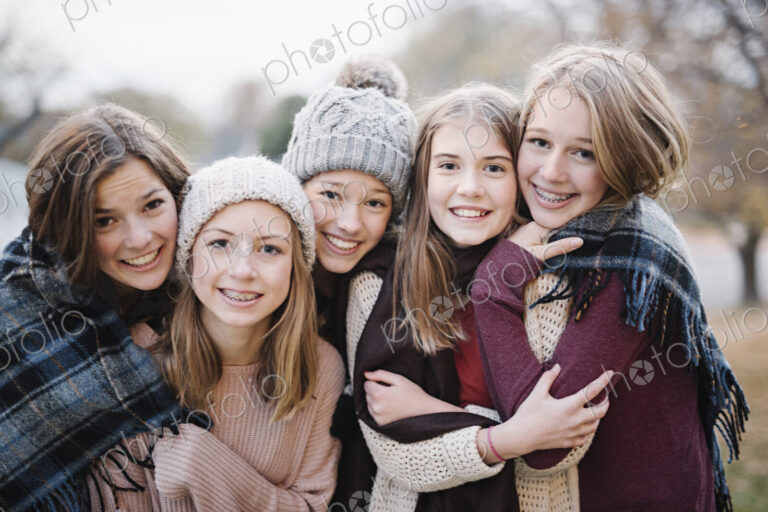 Five young people, girls, friends in warm shawls and woolly hats outdoors.